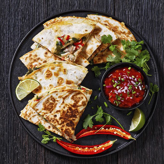 A plate of folded crepes with lime wedges, chile pepper, and sauce. 